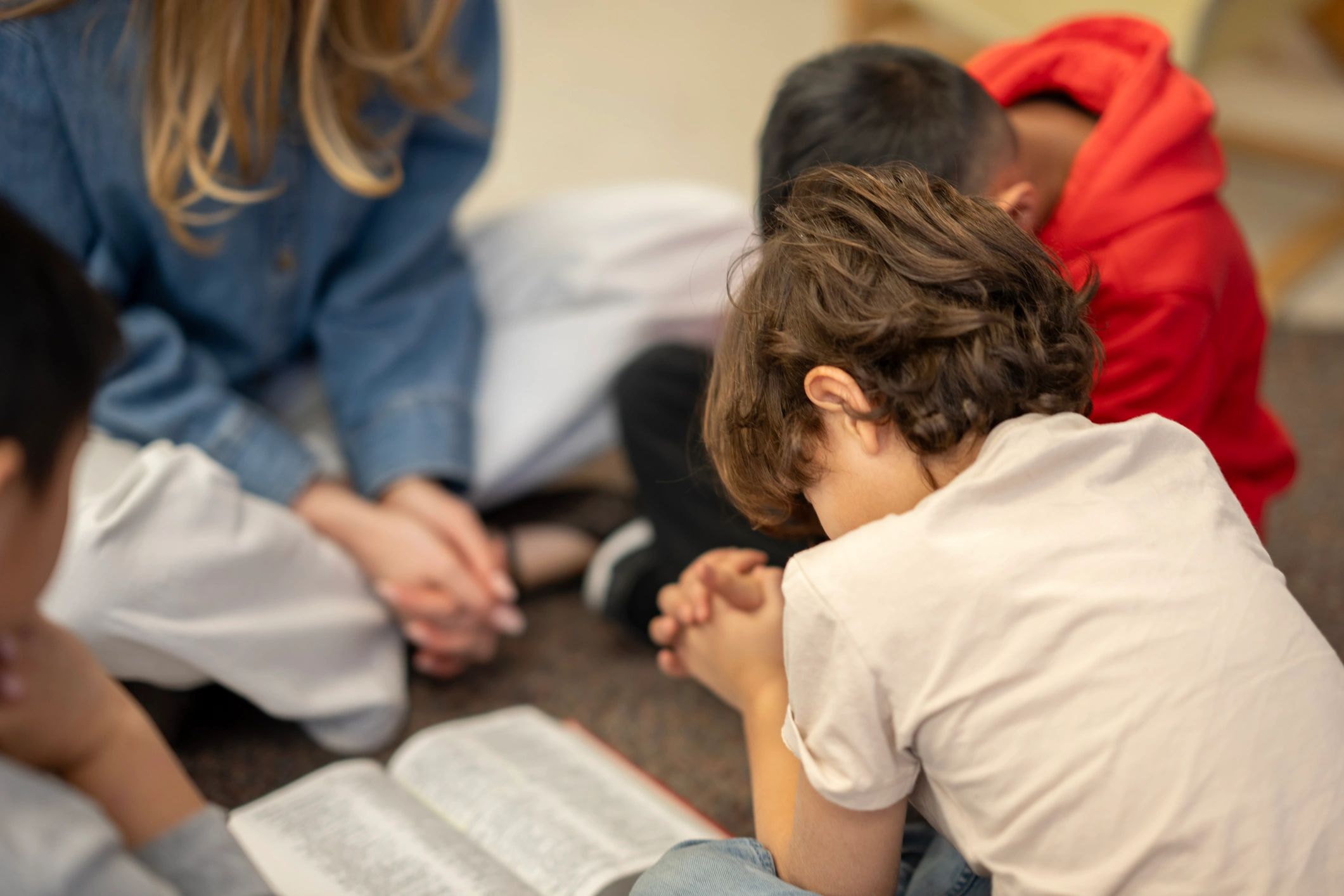 Children praying together around an open Bible